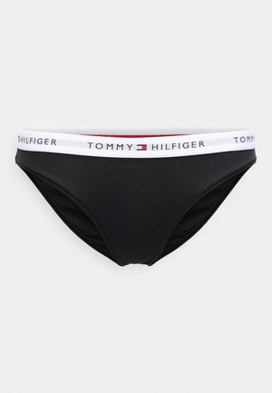 Čierne bikini nohavičky s bielym elastickým pásom, na ktorom je logo "TOMMY HILFIGER" a červený akcent. Hladká látka s priliehavým strihom.