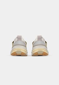 Baskets Nike avec une tige en mesh gris clair, rehaussée d'accents dorés et beiges, semelle en caoutchouc avec adhérence texturée et une languette au talon.