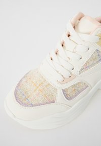 Adidași albi cu umplutură din țesătură texturată, accentuați cu nuanțe pastelate, talpă groasă și închidere cu șireturi. Model croșetat colorat remarcabil pe lateral.