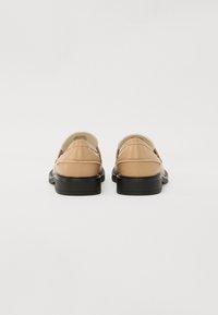 Chaussures en cuir de couleur beige clair avec des semelles noires, présentant une surface lisse et un design à bout rond. La vue arrière montre des détails de couture.