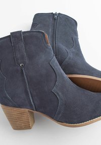 Botine din suede albastru închis, cu toc din lemn texturat, având un fermoar pe lateral și detalii de cusătură curbată pe partea superioară.