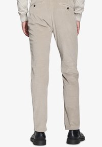 Beige fløjspants med slim fit, to baglommer med knapper og et struktureret stof. Båret med sorte sko.