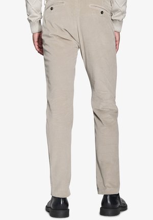 Beige Cordhosen mit schmaler Passform, zwei Gesäßtaschen mit Knöpfen und einem strukturierten Stoff. Getragen mit schwarzen Schuhen.