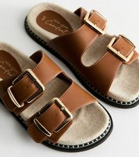 Sandalias de imitación cuero marrón con dos correas anchas, que presentan detalles de hebilla dorada, plantilla de tela beige y suela negra con costuras blancas.