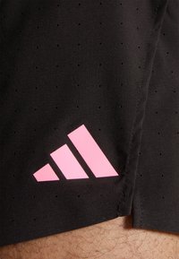 Svarta atletiska shorts med perforerad textur, med en rosa Adidas-logga på nedre vänstra sidan. Tyget är smidigt och lätt.