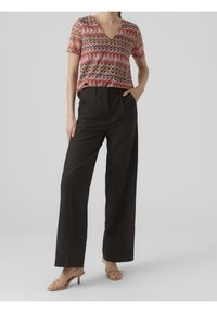 Haut à manches courtes et col en V avec motif zigzag multicolore ; associé à un pantalon large noir taille haute et des sandales à talons couleur nude.