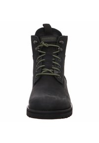 Bota de cuero negra con cordones verdes, ojales metálicos y un collar acolchado. Cuenta con una suela texturizada y un sutil logotipo en la lengüeta.