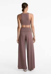 Mauve träningsklädesset med en åtsittande racerback crop-top och vida högmidjade byxor gjorda av mjukt, elastiskt material.
