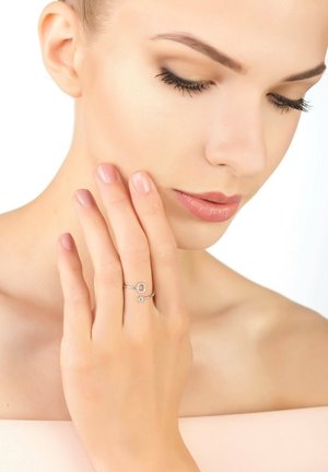 Silver ring with circular and gemstone accents worn on a hand, featuring smooth skin and neutral-colored nails against a light background.