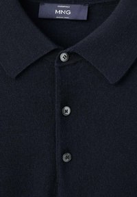 Granatowa koszulka polo z merynosowej wełny, z klasycznym kołnierzykiem, ozdobiona trzema małymi, ciemnymi guzikami wzdłuż listwy. Miękka, teksturowana tkanina.