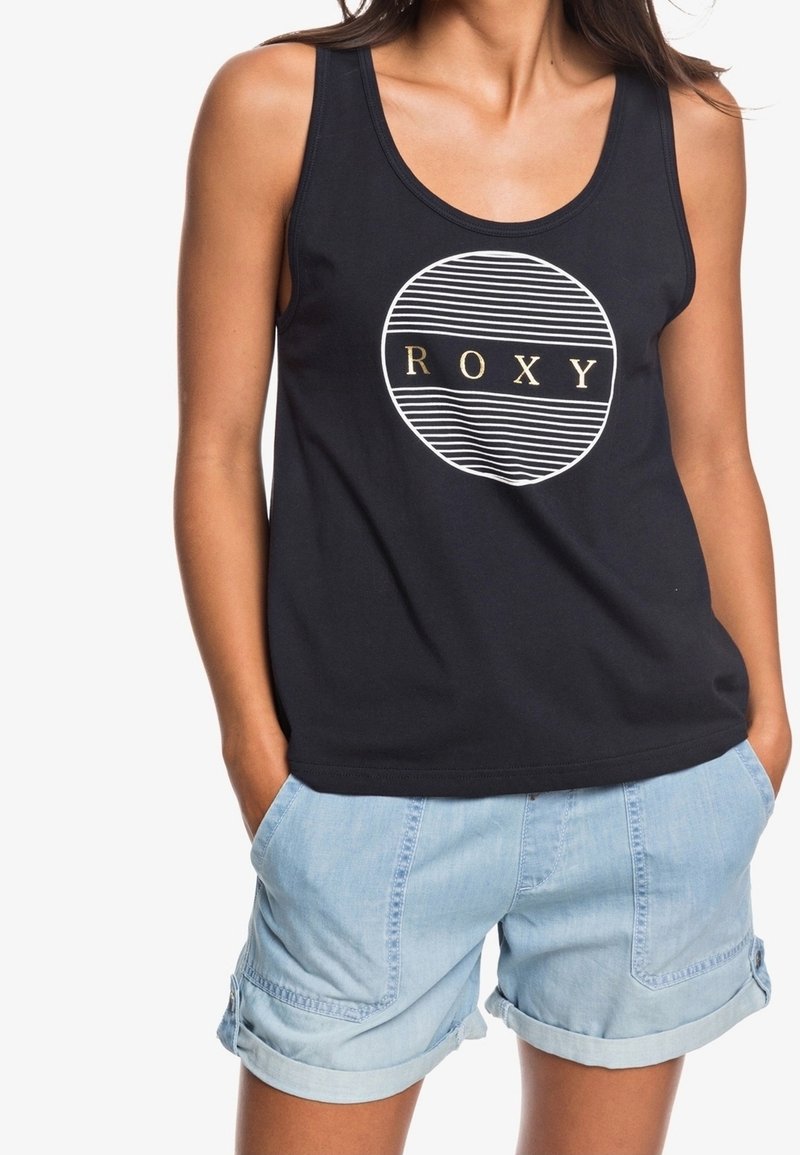 Zwart tanktop met een wit-gouden ronde logo met strepen, gecombineerd met lichtblauwe denim shorts met opgerolde boorden.