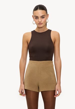 Bruine mouwloze top met hoge hals, gecombineerd met beige fluffy shorts, die een gladde textuur en een aansluitende pasvorm hebben.