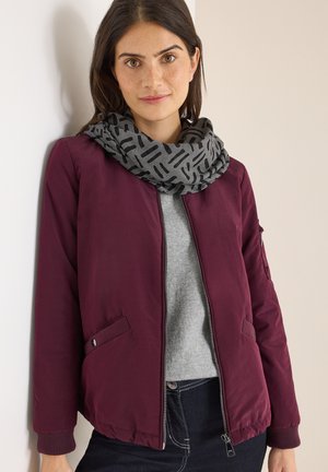 Veste bomber bordeaux avec des poignets côtelés, pull gris en dessous et une écharpe grise à motifs avec des lignes noires. Fini en tissu lisse.