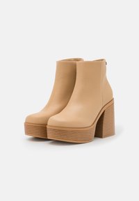Beige nahka nilkkurit, joissa on sileä pinta, neliömäinen kärki ja erottuva raidallinen puinen korko. Rentoa muotoilua, jossa on vain vähäisiä yksityiskohtia.