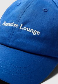 Plava pamučna kapa s izvezbom loga "Executive Lounge" u bijeloj boji. Ima zakrivljeni vizir i ojačane šavove.
