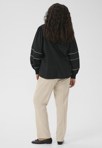 Blouse noire à manches longues avec manches froncées ornées de rayures horizontales blanches, associée à un pantalon beige et des ballerines noires.