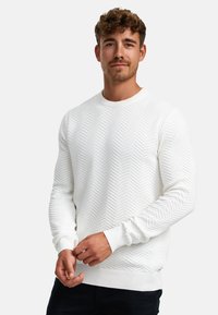 Hvit strikket genser med en strukturert fiskebensmønster, ribbestrikkede mansjetter og nederkant, rund halsutringning og lange ermer.