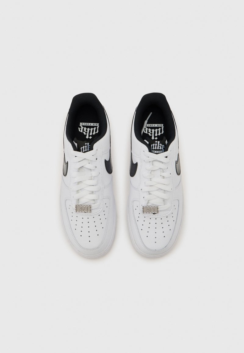 Paire de baskets Nike Air Force 1 blanches avec logos swoosh noirs, lacets blancs et orteils perforés, vues de dessus sur un fond clair.