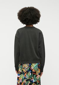 Sweatshirt côtelé gris foncé avec une coupe décontractée et un col rond, associé à une jupe à motif floral coloré. Aucun matériel ou accent visible.