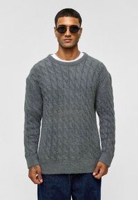 Grijze kabelgebreide sweater met een losse pasvorm, ronde halslijn en geribde manchetten. Zachte textuur en variërende breipatronen.
