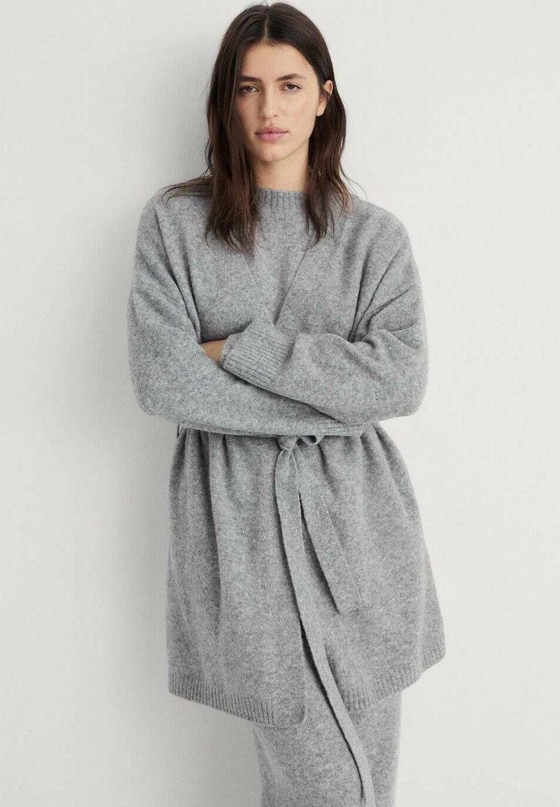 Cardigan tricoté gris clair avec une ceinture à nouer, des manches larges et une coupe décontractée. Texture douce et accents côtelés subtils au niveau des poignets.