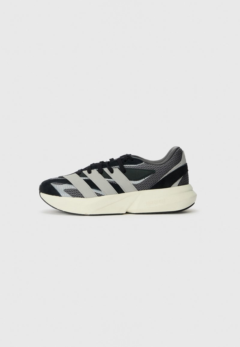 Chaussure de sport noire et grise en matériaux en mesh et en suède, dotée de trois bandes horizontales, d'une semelle épaisse et d'un motif texturé.