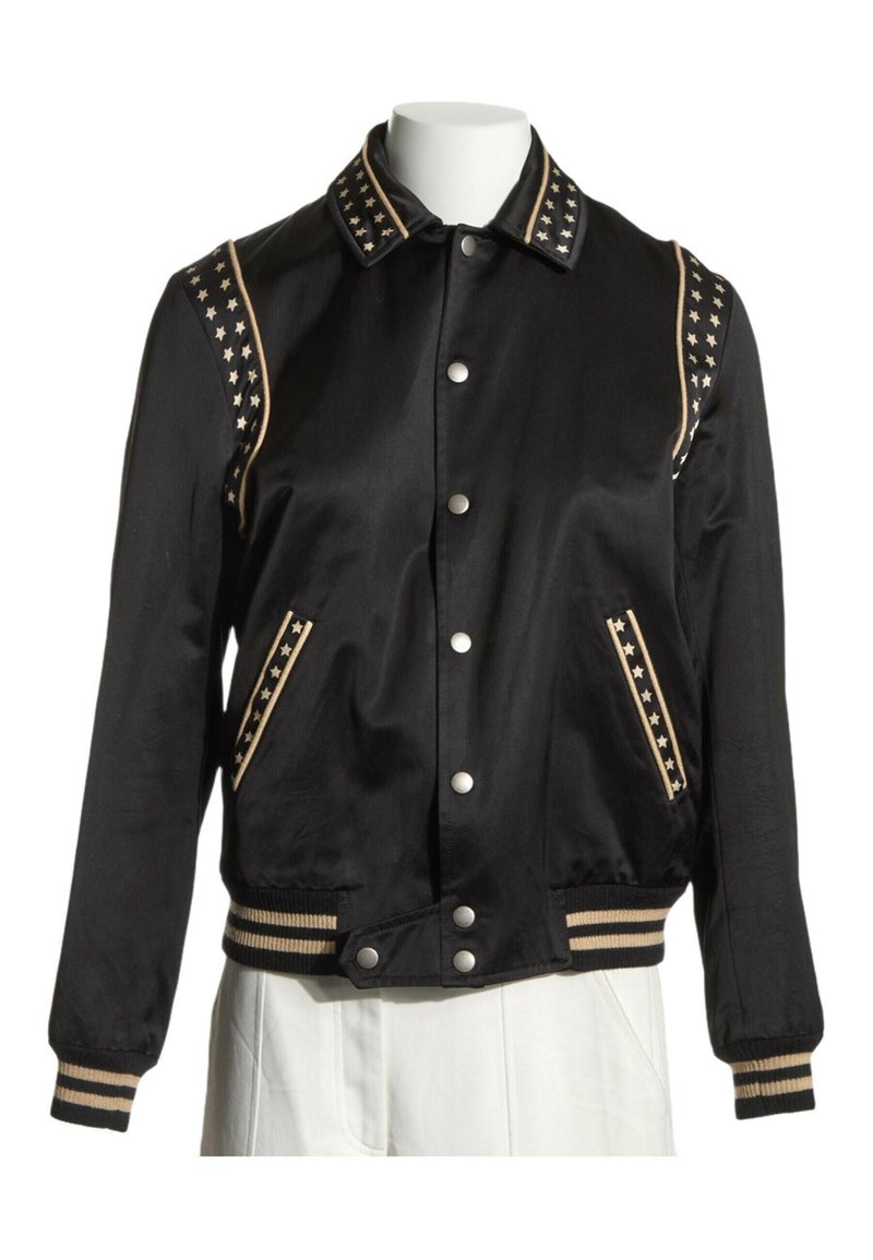 Veste bomber en satin noir avec des accents d’étoiles dorées sur le col, les épaules et les poches, des poignets et une ceinture rayés, et des boutons-pression argentés.