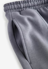 Grå sweatpants med elastisk talje, sidelommer og et blødt, struktureret stof. Har en afslappet pasform og flade sømme.