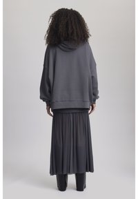 Sweatshirt gris surdimensionné avec une finition texturée, associé à une longue jupe noire transparente, superposée sur un pantalon noir slim.