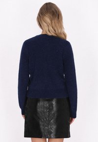 Suéter de punto azul marino con textura de acanalado, con un escote redondo y mangas largas, combinado con una falda de cuero negro brillante.