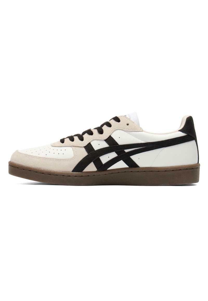 Niskie białe sneakersy z beżowymi zamszowymi panelami, czarnymi bocznymi paskami, czarnymi sznurówkami i brązową gumową podeszwą, pokazane w widoku bocznym.