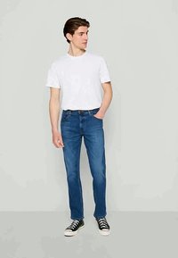 Vit kortärmad t-shirt i kombination med blå raka jeans och svarta sneakers. Outfiten har en avslappnad passform och klassisk design.