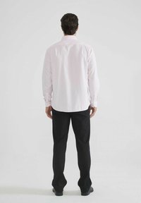 Chemise rose clair à manches longues avec col boutonné, associée à un pantalon noir. Tissu lisse avec une coupe classique, sans motifs visibles.