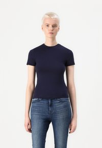 Mørk blå kortermet t-skjorte med rund hals, tettsittende design, laget av glatt stoff. Brukt sammen med lyse denimjeans.
