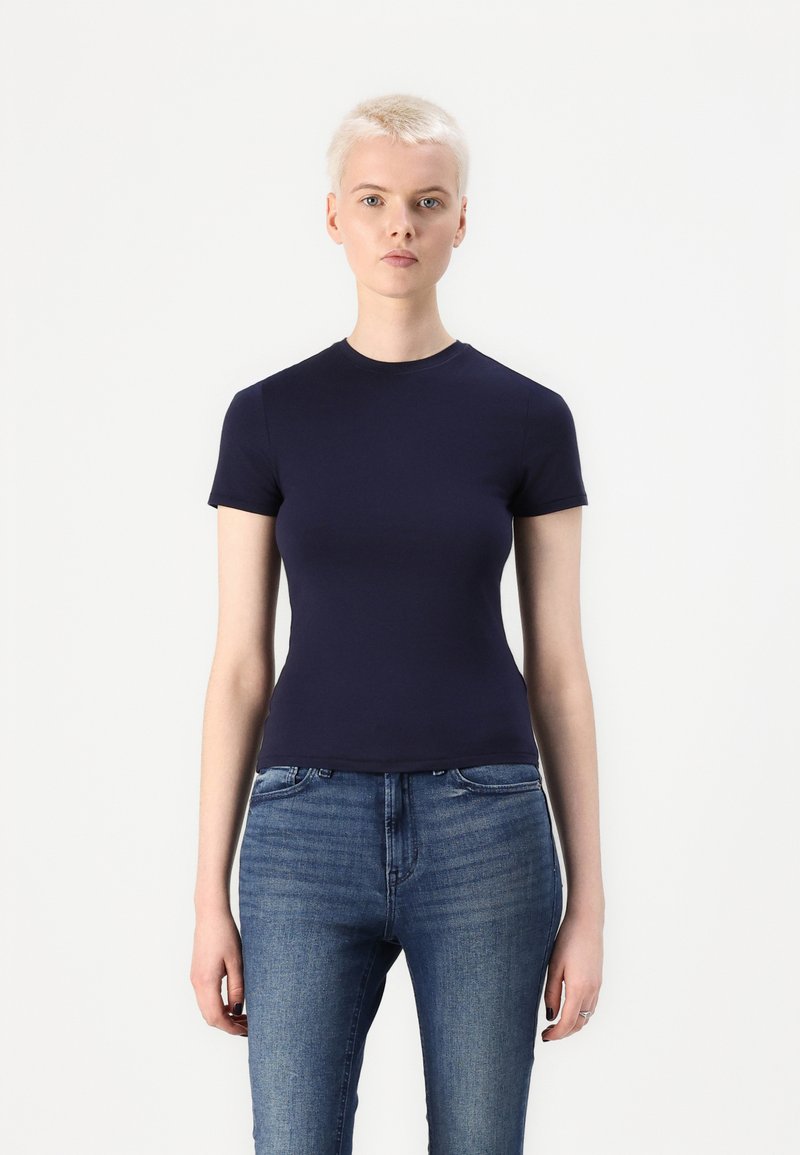 Mørk blå kortermet t-skjorte med rund hals, tettsittende design, laget av glatt stoff. Brukt sammen med lyse denimjeans.