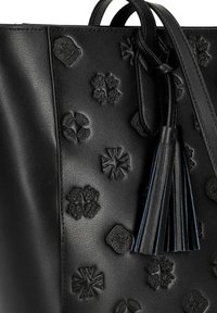Borsa a mano in pelle nera con motivi floreali e geometrici stampati in rilievo, con un dettaglio a nappina appesa alla tracolla. Tessuto liscio.