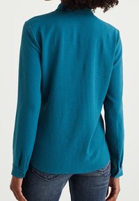 Blauwe overhemd met lange mouwen, voorzien van een gestructureerde afwerking, knoopmanchetten en een ronde onderkant. De stof lijkt soepel en licht van gewicht.