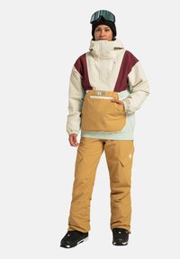 Súprava vonkajšieho oblečenia obsahuje štrkovanú bundu v krémovej, vínovej a mätovej farbe, s prednou kapsou, skombinovanú s pieskovými lyžiarskymi nohavicami a čiernymi topánkami.