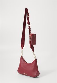 Red faux leather shoulder bag with a curved silhouette, gold hardware, and a detachable matching mini pouch on a velvet strap.
