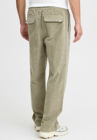 Khakifarbene Cord-Hosen mit elastischem Bund, geradem Bein und zwei Gesäßtaschen. Glatte Textur mit vertikalen Rippdetails.