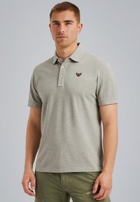 Camisa polo gris con una tapeta de dos botones, mangas cortas y un pequeño emblema bordado en el lado izquierdo del pecho. Tejido ligeramente texturizado.