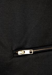 Black fabric with a smooth texture, featuring a visible gold zipper along the seam. The zipper is partially open, revealing the interior.