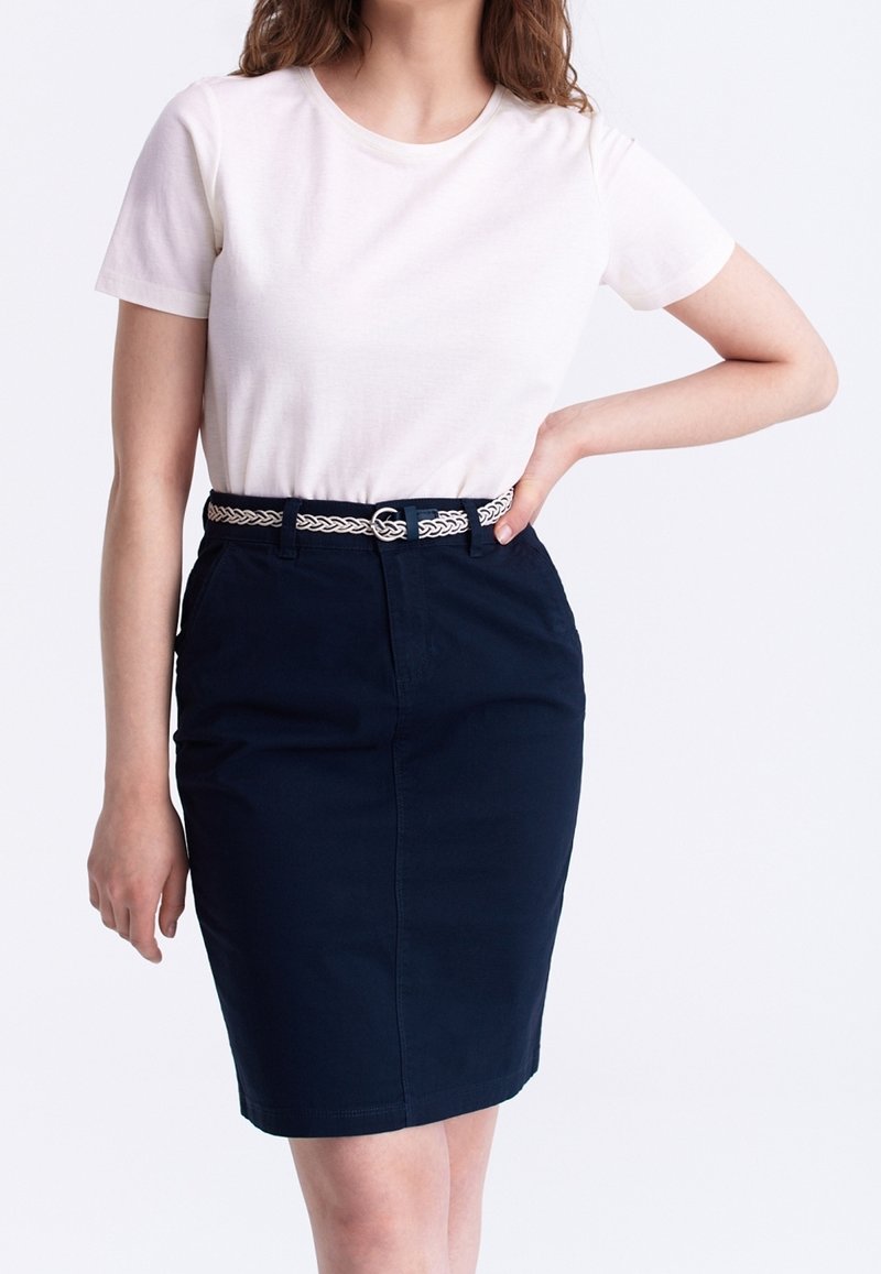 T-shirt en coton blanc associé à une jupe crayon bleu foncé. La jupe est ornée d'une ceinture tressée avec une boucle ronde.