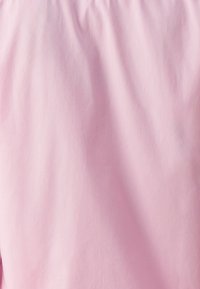 Vaaleanpunainen kangas, jossa on sileä pinta, pehmeitä taitoksia ja elastinen yläreuna. Yksinkertainen, minimalistinen muotoilu ilman näkyviä kuvioita.