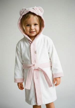 Young girl smiling, wearing a white and pink hooded bathrobe with bear ears and a flower detail, standing against a plain background.