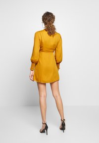 Senapsgul mini klänning med långa puffärmar, smockade manschetter och en figursydd midja. Stylande med svarta klacksandaler.