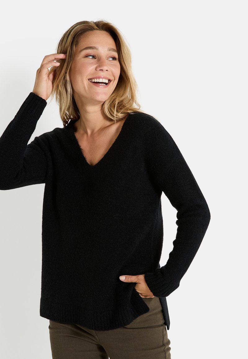 Suéter negro de punto con cuello en V, mangas largas, puños acanalados y un ajuste relajado, combinado con pantalones verde oliva. Textura suave y diseño casual.