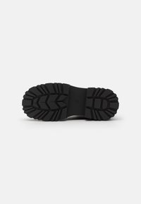 Semelle de botte en caoutchouc noir avec un motif de semelle texturé, conçu pour l'adhérence et la durabilité, avec des rainures définies et une forme robuste.