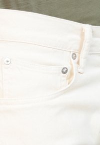 Pantalones de mezclilla blanca con un bolsillo frontal, herrajes plateados en la cinturilla y textura de costura visible.