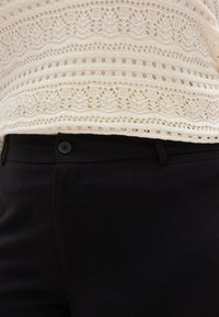 Πλεκτό κρεμ τοπ με σχέδιο δαντέλας, συνδυασμένο με μαύρο παντελόνι ραμμένο στο μέτρο, με κλείσιμο με κουμπί και λεία υφή.